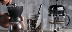 A person hand grinding coffee beans near a jar of beans and French Press 