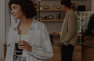 Woman leaving coffeebar with to-go cup with a man shopping in the background