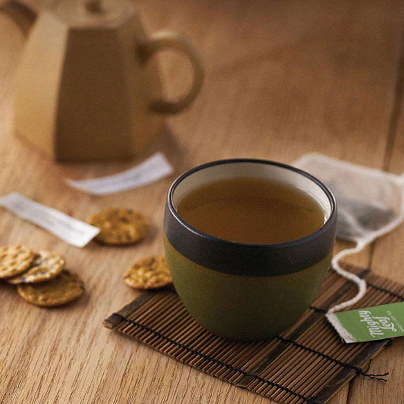 Tea cup with a phone, cookies, and teapot on a wooden table