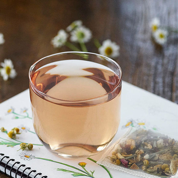 Glass of tea on a notebook with flowers and a pencil on a wooden surface
